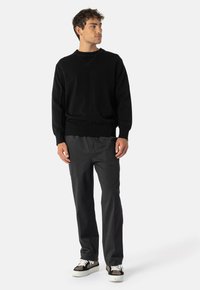 Černý pletený svetr s výstřihem do V a žebrovanými manžetami, spárovaný se šedými kalhotami rovného střihu a černými teniskami s bílými akcenty.