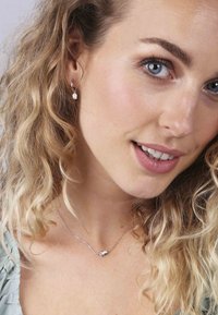 Bijoux en argent comprenant des boucles d'oreilles en forme de feuilles et un collier assorti. Le design est délicat, avec des chaînes fines et des accents polis.