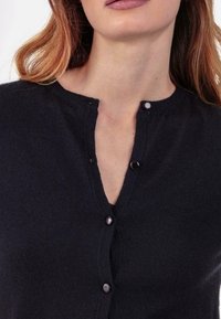 Schwarzer Cardigan mit V-Ausschnitt und dezenter Knopfleiste, gefertigt aus weichem Stoff mit strukturierter Oberfläche.