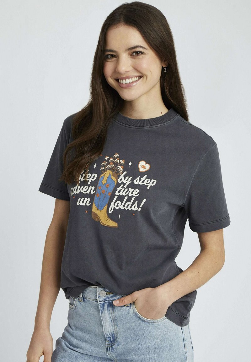T-shirt gris graphique avec une illustration de bottes colorées et du texte. Manches courtes, col rond, coupe décontractée et en coton.