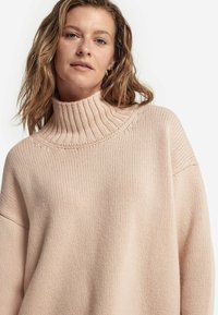 Jasnoróżowy, dziany sweter z wysokim prążkowanym kołnierzem, luźny krój i widoczny teksturowany wzór. Miękka, średniej wagi tkanina.