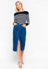Top de rayas azul marino y blanco de manga larga combinado con una falda de mezclilla azul hasta la rodilla, con una abertura frontal y bolsillos laterales, llevado con tacones transparentes.