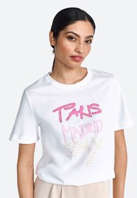 Tricou din bumbac alb, cu un text colorat din strasuri care spune "PARIS MADRID" în roz și auriu. Mâneci scurte și guler rotund.