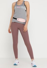 Top in canna di fucile con strisce rosa e blu, abbinato a una borsa in vita rosa. Leggings marroni a coste e sneakers bianche con dettagli blu e rosa.