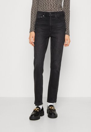 Kvinde iført sorte jeans med høj talje, langærmet top med bølgede striber, hvide sokker og sorte loafers med guldkædedetalje.