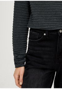 Temno siva rebrasta majica z dolgimi rokavi s skrajšanim dizajnom, v kombinaciji z visokim pasom črnimi jeans hlačami, ki imajo sprednji žep in podrobnosti z srebrnim gumbom.