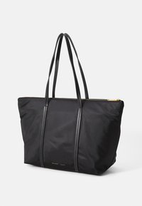 Saco tote de nylon preto com alças de couro duplas, fecho de zíper dourado e detalhe do logótipo em relevo discreto na frente. Textura suave e lisa.