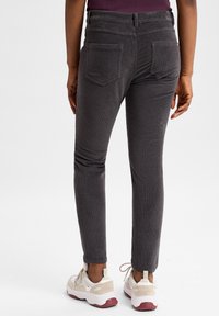 Grijze corduroy broek met een slim fit, voorzien van achterzakken en een tailleband. Gepaard met witte en roze sneakers.