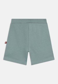 Green cotton shorts with a soft texture, elastic waistband, and a small red brand tag on the left side. Smooth, straight-cut design.