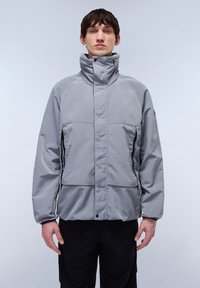 Padded grey jacket with high collar, side pockets, and front snap closures. Smooth texture with contrasting seam detailing.