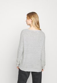 Hellgrauer Strickpullover mit lockerer Passform, weit geschnittenem Halsausschnitt und langen Ärmeln. Die Textur ist weich und leicht locker, mit einem längeren Rückensaum.