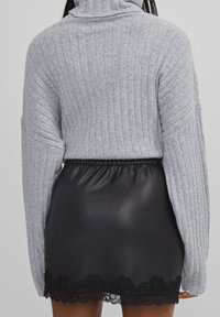 Grå ribbad polotröja med långa ärmar, tillsammans med en svart fusk läderkjol med spetstyg vid fållen.