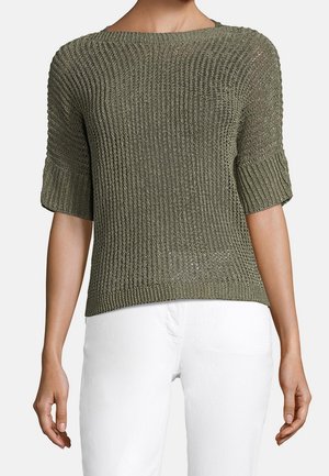 Olivengroene gebreide trui met brede halslijn en opgerolde ellebooglange mouwen, gedragen met witte broek.