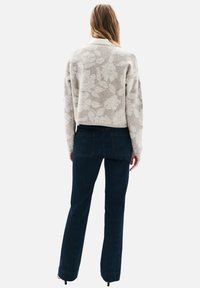 Pull gris clair avec motif floral, poignets et ourlet côtelés, associé à un jean en denim foncé avec jambes droites et coutures minimales.
