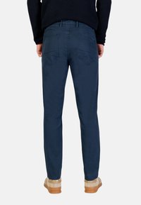 Pantaloni chino blu navy con design a gamba dritta, caratterizzati da una parte frontale liscia e due tasche posteriori, abbinati a scarpe beige.