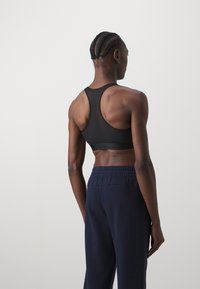 Black sports bra with a racerback design, featuring a smooth texture and elastic band. Model wears navy sweatpants, viewed from the back.