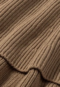 Brauner gerippter Strickstoff mit weicher Textur, der vertikale Linien und einen leicht gewellten Rand aufweist. Keine sichtbaren Muster oder Beschläge.