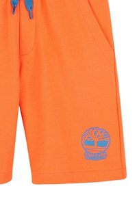 Pantaloni corti arancioni brillanti realizzati in tessuto testurizzato, con una coulisse blu e un logo circolare blu Timberland sul lato sinistro.