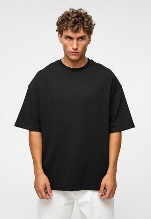 Zwarte oversized t-shirt gemaakt van katoen, met een ronde hals, korte mouwen en een relaxte fit, in combinatie met witte broeken.