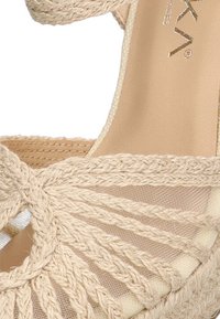 Sandalia espadrille trenzada de color beige con diseño de parte superior trenzada que presenta una textura natural y un forro de tela suave. Incluye un tacón bajo tipo cuña.