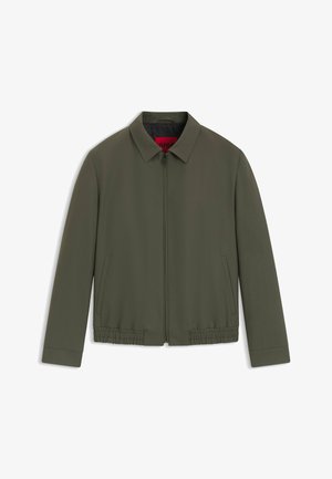 Oliivivihreä takki, jossa on kauluksellinen kaula-aukko, etuvetoketju, sivutaskut ja joustava helma. Valmistettu sileästä, kevyestä kankaasta.