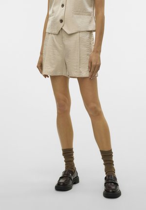 Beige textuur shorts en bijpassend vest gedragen met bruine opgerolde sokken en donkerbruine leren loafers bij een staande persoon.