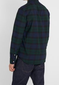 Camicia a quadri button-up in verde scuro e blu navy, con maniche lunghe, colletto classico e orlo curvo. Il tessuto sembra liscio con una leggera lucentezza.