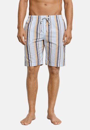 Man met knielange zwembroek met verticale strepen in blauw, wit, oranje en grijs, staand op blote voeten tegen een witte achtergrond.