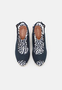 Escarpins à talons compensés bleu marine avec un bout ouvert, extérieur en tissu et intérieur à motifs présentant des feuilles blanches. Détail de lanière à boucle au niveau du talon.