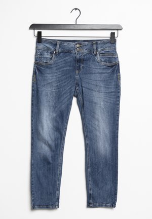 Jean en denim bleu avec des détails délavés, fermeture double bouton à l'avant et cinq poches, suspendu sur un cintre noir sur fond blanc.