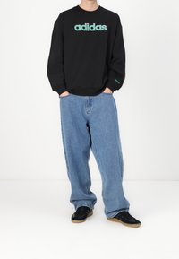 Svart sweatshirt med turkos "adidas"-logotyp, matchad med ljusblå baggy jeans och svarta sneakers med gummisulor. Slät tyg och avslappnad design.