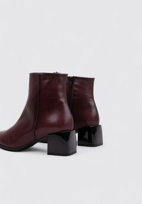 Bottines en cuir bordeaux au fini lisse, avec un talon bloc noir et une fermeture éclair à l'arrière.