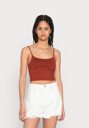 Top cropped ajustado de cor vermelha enferrujada com alças finas, combinado com calções de ganga brancos de cintura alta com bordas desfiadas e bolsos frontais.