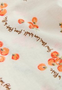 Tissu blanc avec de petits motifs floraux et fruités orange et un texte cursif marron dispersé sur la surface.