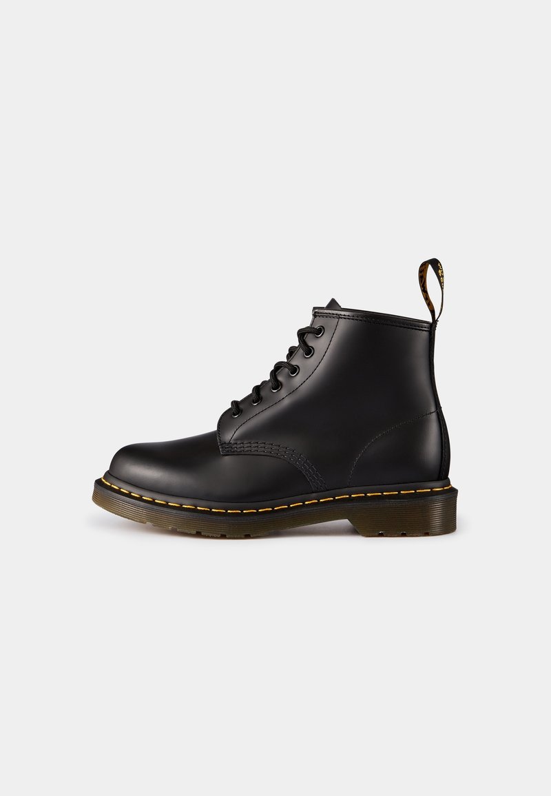 Bottine en cuir noir à lacets avec surpiqûres jaunes, une semelle épaisse translucide et une languette de tirage marquée à l'arrière.