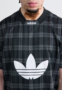 Juodas ir pilkas languotas trumpas rankovėmis marškinėliai su juodu apykakle, frontinėje pusėje išryškintas baltas Adidas trefoil logotipas.