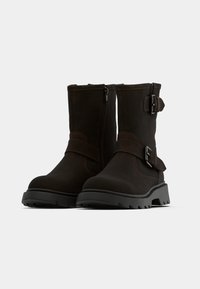 Botines marrones de material texturizado, con cremallera lateral, adorno de hebilla y suela robusta con un ligero tacón.