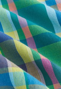 Tissu coloré à motif à carreaux en bleu, vert, jaune, violet et rose, montrant des plis et des détails de tissage texturé.