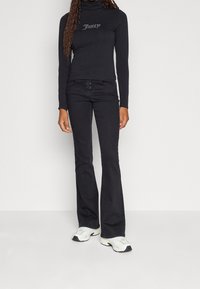 Black turtleneck top with "Juicy" text, paired with fitted black flared jeans and white athletic shoes with black accents.