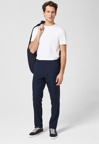 Witte t-shirt gecombineerd met marineblauwe broek en donkere sneakers, met een marineblauwe blazer over één schouder gedrapeerd. Glad materiaal, op maat gesneden pasvorm.
