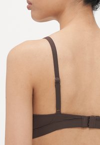 Brown bra with adjustable straps, a hook closure, and smooth fabric. The back features a simple design with a solid texture.