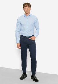 Light blue striped shirt with a collar, paired with dark navy slim-fit pants. Satin finish black shoes complete the look.