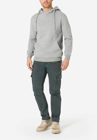 Grauer Baumwollhoodie mit einer Kängurutasche und Kordeln, kombiniert mit dunkelgrünen Cargo-Hosen mit Seitentaschen und beigen Sneakern.