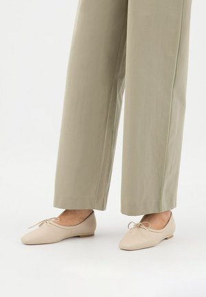 Beige baletní lodičky s vykrojenou špičkou, plochým podpatkem a dekorativní mašlí. Hladký materiál s jednoduchým designem, v kombinaci se světle zbarvenými širokými kalhotami.