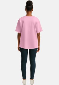 T-shirt oversize rosa con maniche corte, scollo rotondo e texture liscia, abbinata a jeans skinny scuri e sneaker bianche.