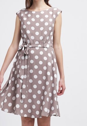 Mouwloze lichtbruine jurk met grote witte stippen, een gestrikte tailleband en een zwierige rok tot op de knie.