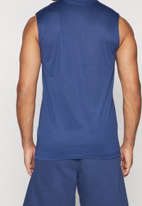 Maglietta sportiva senza maniche di colore blu navy realizzata in tessuto morbido; presenta un colletto rotondo e una vestibilità comoda. La vista posteriore mostra cuciture piatte e nessun ornamento.