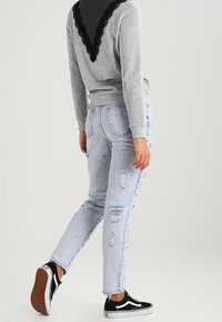 Sudadera gris con encaje negro en la parte posterior, combinada con jeans desgastados de color azul claro y zapatillas negras con detalles blancos.