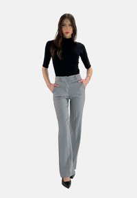 Pantalon gris ajusté avec une taille haute et des jambes larges, arborant un motif à carreaux subtil. Associé à un haut col roulé noir ajusté.