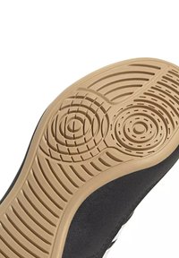 Semelle d'une chaussure noire avec une semelle extérieure en caoutchouc beige présentant des motifs circulaires et linéaires pour l'adhérence.